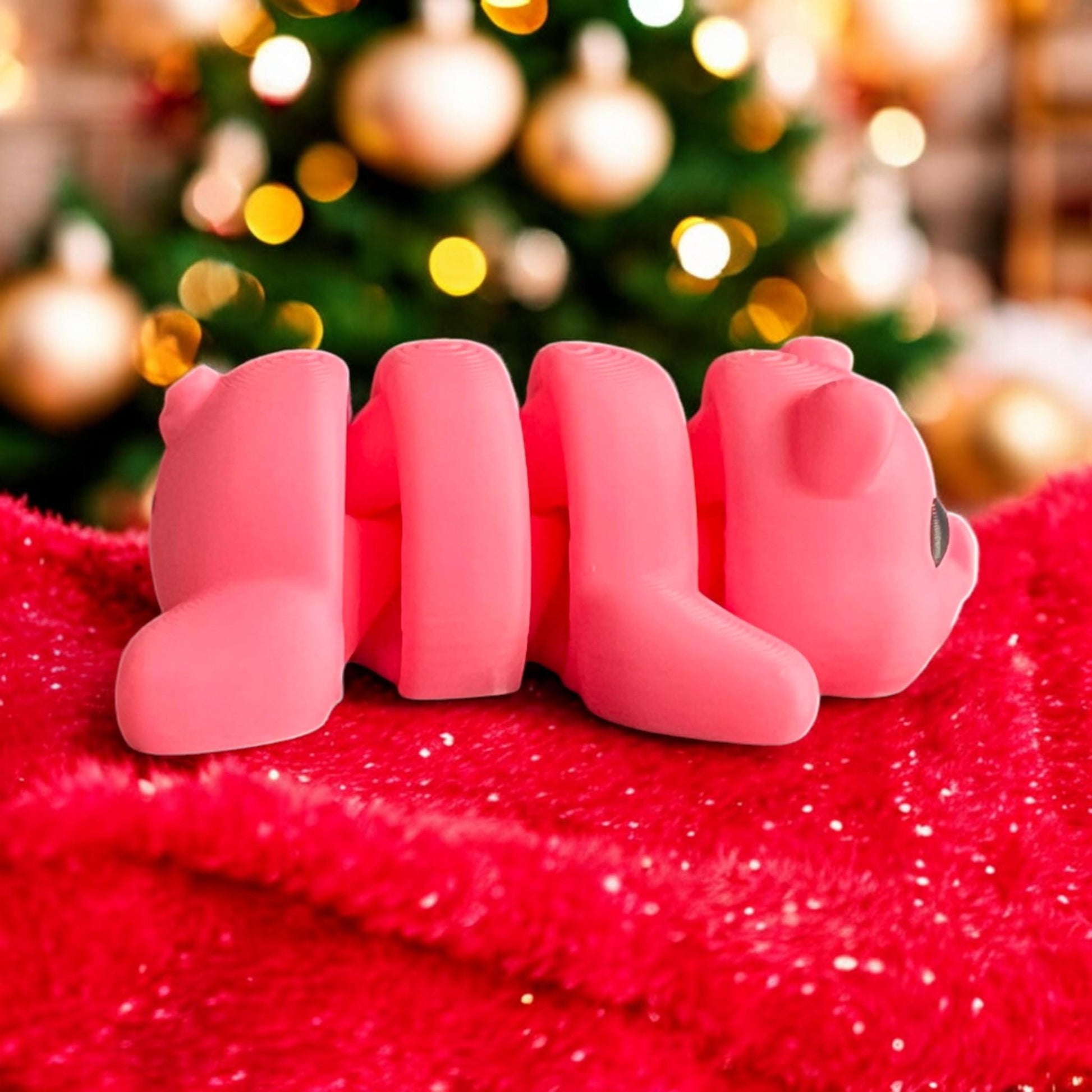Side view of a pink 3D printed articulated baby pig lying on a red glittery blanket, with a beautifully lit Christmas tree and festive ornaments in the background, perfect for capturing the holiday spirit
