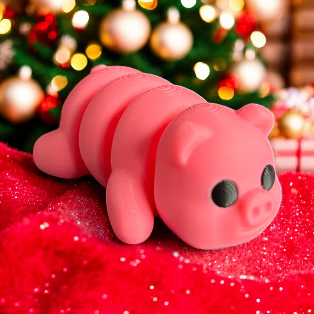 A cute 3D printed pink articulated baby pig posed on a red festive blanket, set against a Christmas tree with glowing lights and ornaments. The pig&#39;s adorable face and big black eyes add charm to the holiday setting