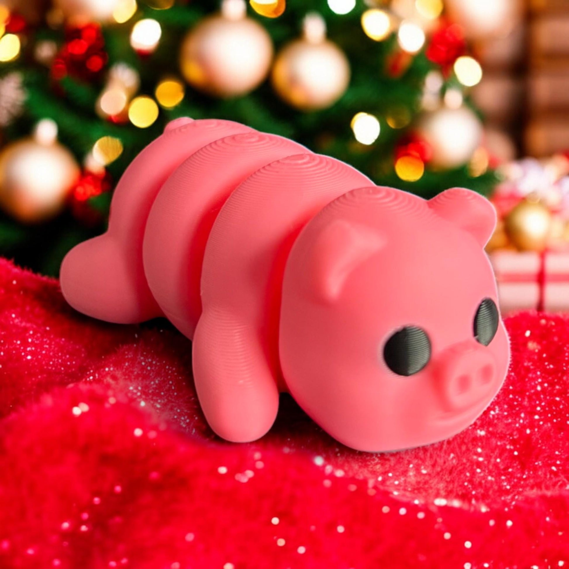 A cute 3D printed pink articulated baby pig posed on a red festive blanket, set against a Christmas tree with glowing lights and ornaments. The pig&#39;s adorable face and big black eyes add charm to the holiday setting
