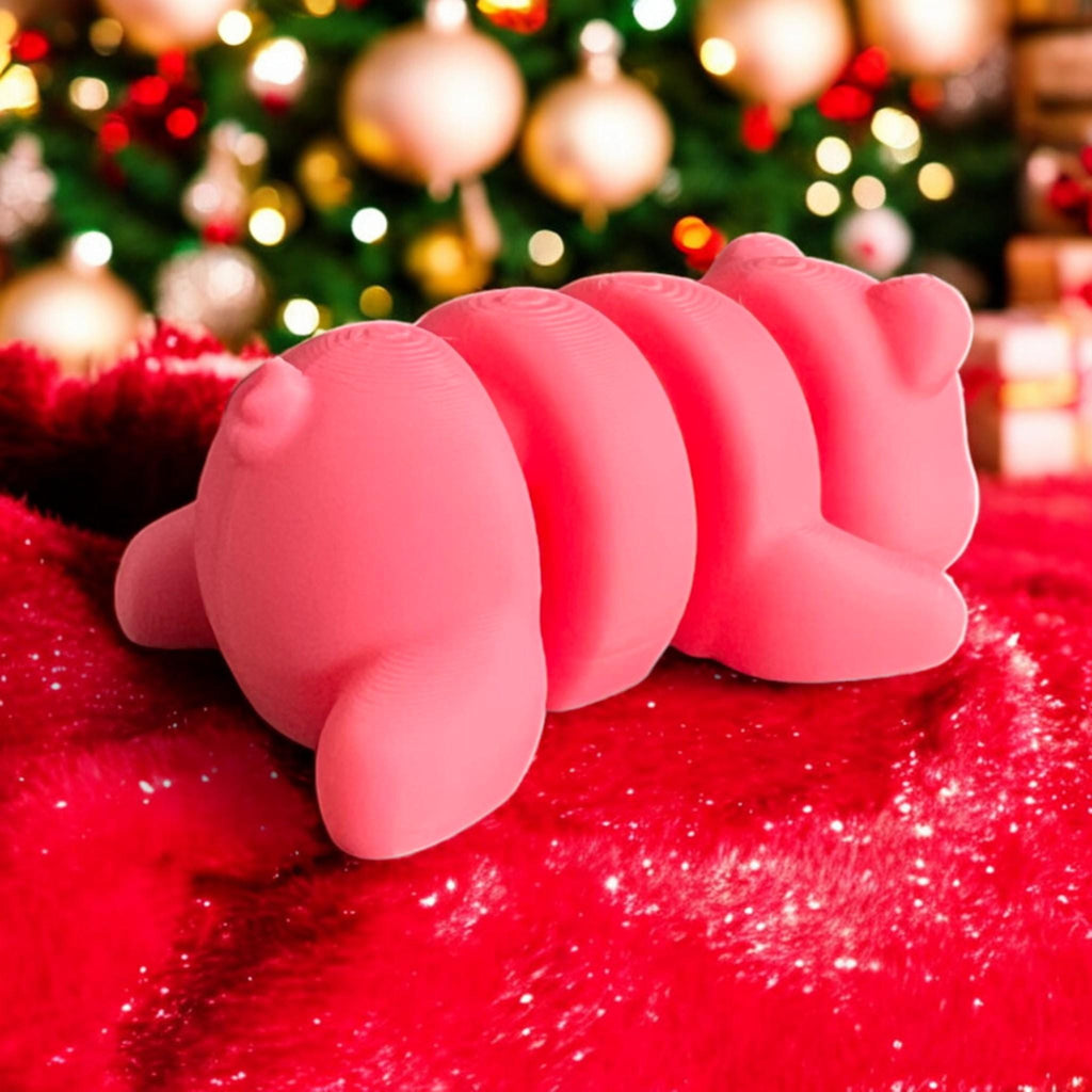 Back view of a 3D printed pink baby pig with a curly tail, resting on a red sparkly surface, with a Christmas tree, glowing ornaments, and wrapped presents adding a cheerful festive vibe