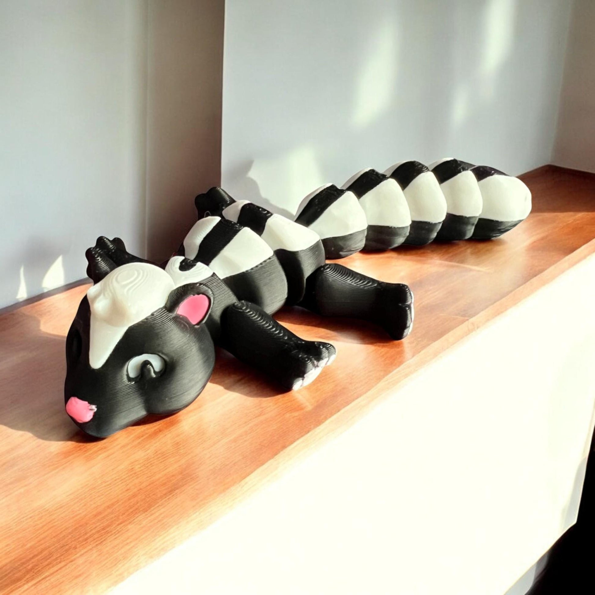 Front view of a 3D-printed black and white articulated skunk fidget toy, showcasing its cute design with a flexible segmented body